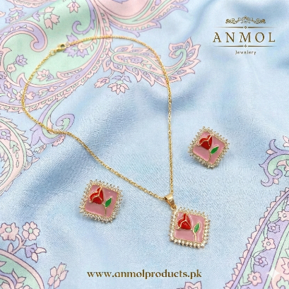 Jewelry set with pink floral pendants on a decorative fabric background, featuring the brand 'Anmol'.