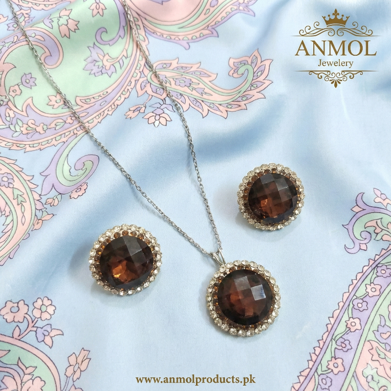 Jewelry set with pendant and earrings on a decorative fabric background, featuring the brand 'ANMOL Jewelry'.