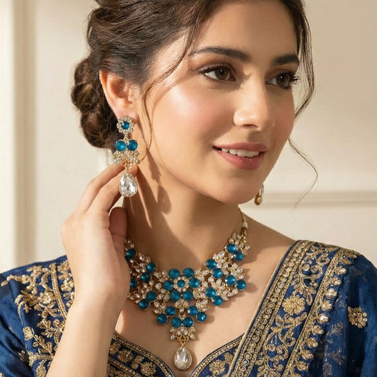 Woman wearing a blue and gold embroidered outfit with jewelry, including earrings and a necklace.