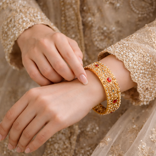Close-up of a hand wearing a gold bracelet with red stones, against a matching fabric background.
